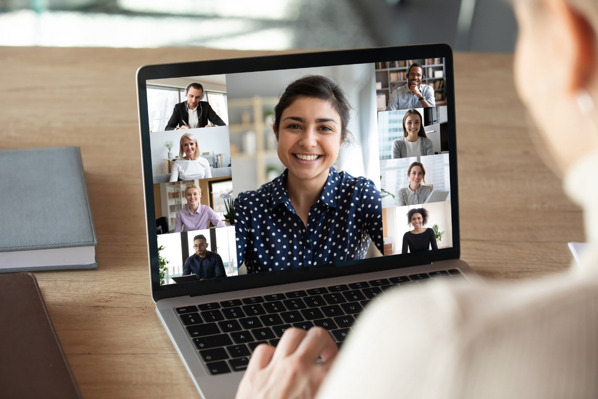 Laptop screen over woman shoulder view during group online communication.