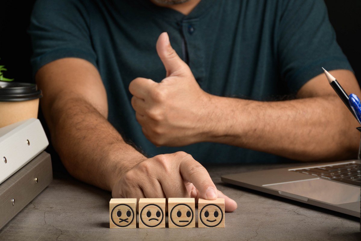 Male person touches feedback with smile wood cube face.