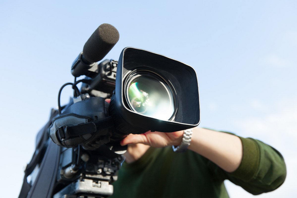 Male videographer holding broadcasting camera.