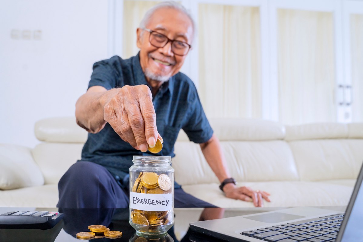 Old man putting coins inside emergency funds jar.