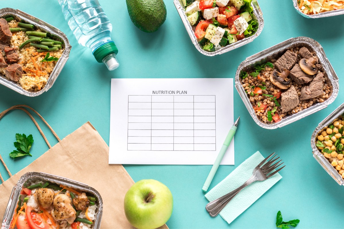 Paper with nutrition plan surrounded by different healthy foods.
