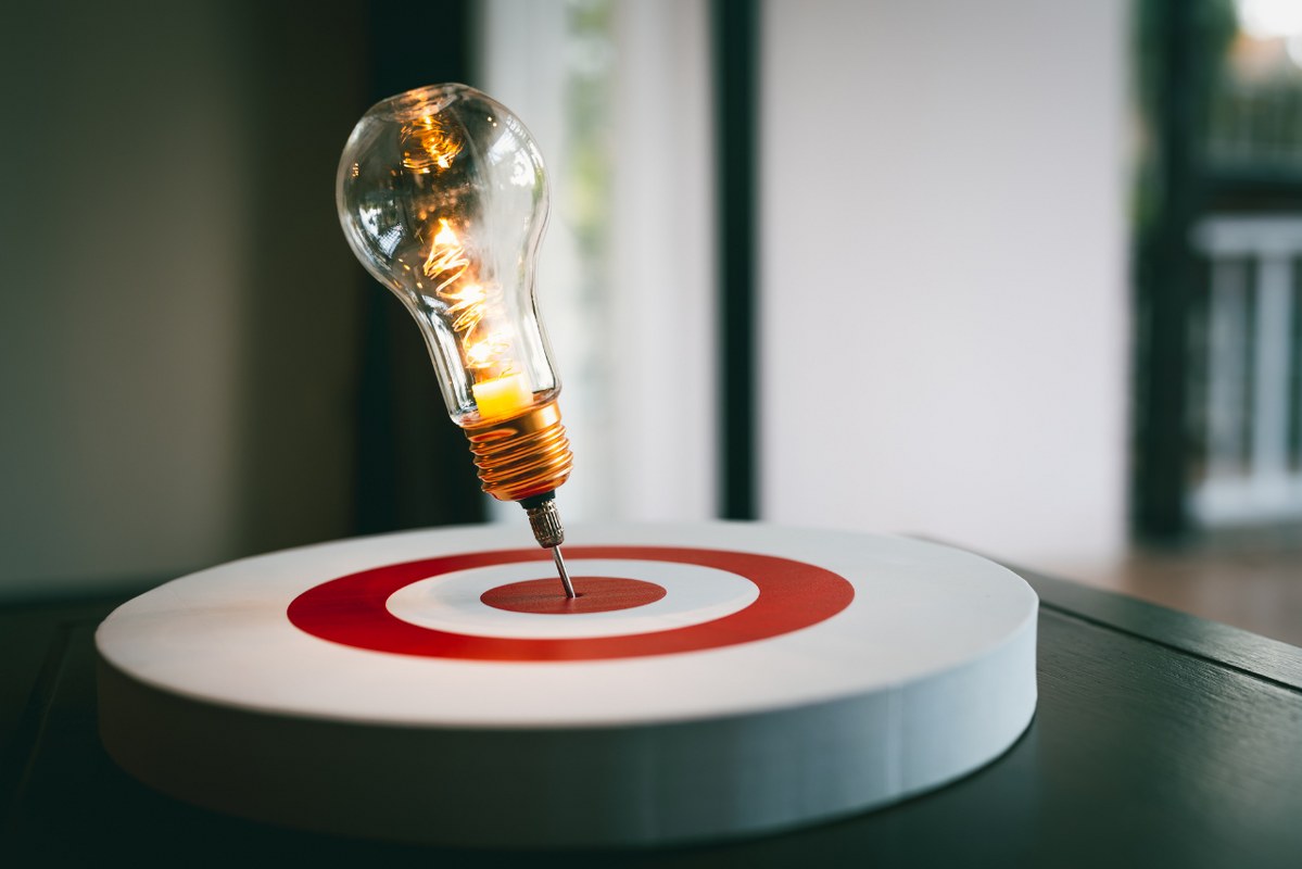 Problem-solving concept: Light bulb with arrow of darts on dart board.