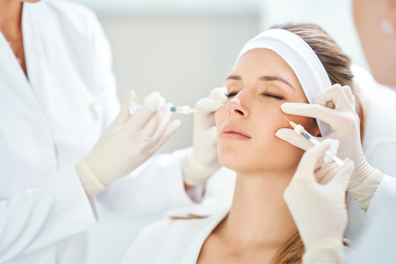 Two female cosmetologists injecting botox to woman.