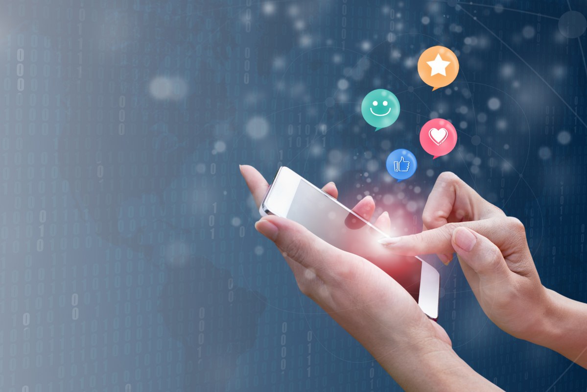 Woman hands pressing smartphone with smiley, heart and emoticons floating on top.