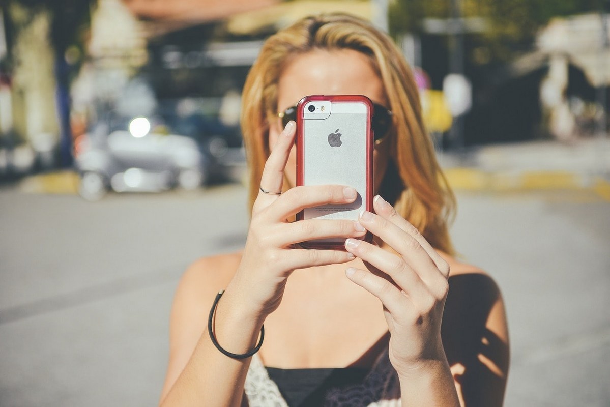 A girl takes a photo with an Apple phone which is considered to be having a premium brand position.