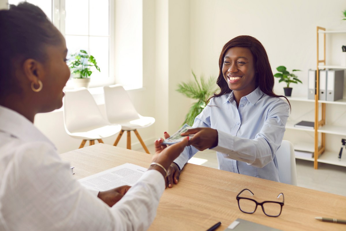 A happy, smiling woman giving cash money to a family member.