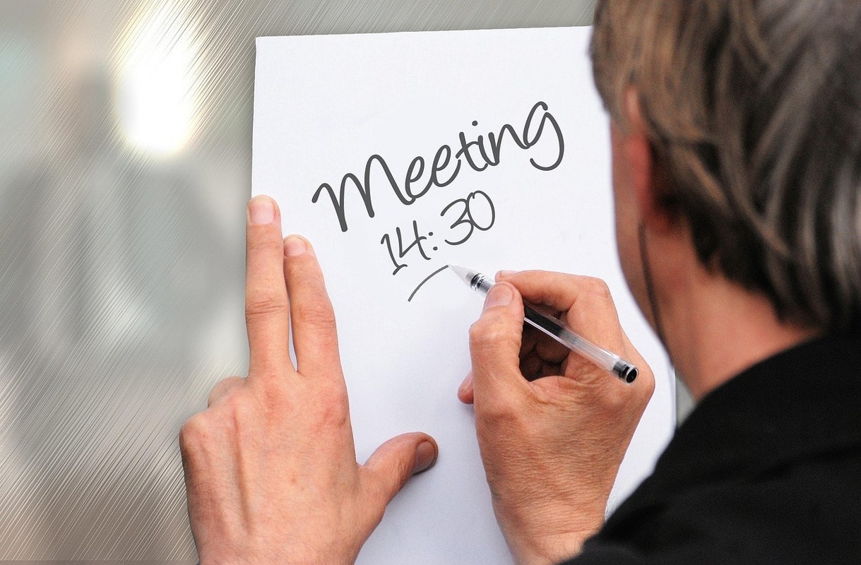 A person writing a memo about a meeting's schedule.