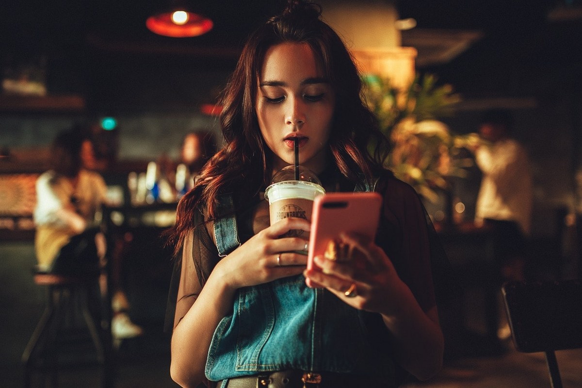 A woman operating her phone while drinking coffee.