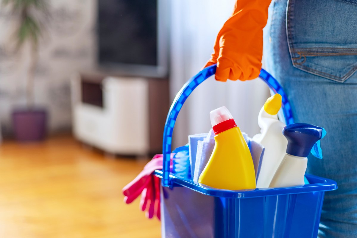 Backview of lower part of a person with rubber gloves with bucket of cleaning supplies ready to clean up.
