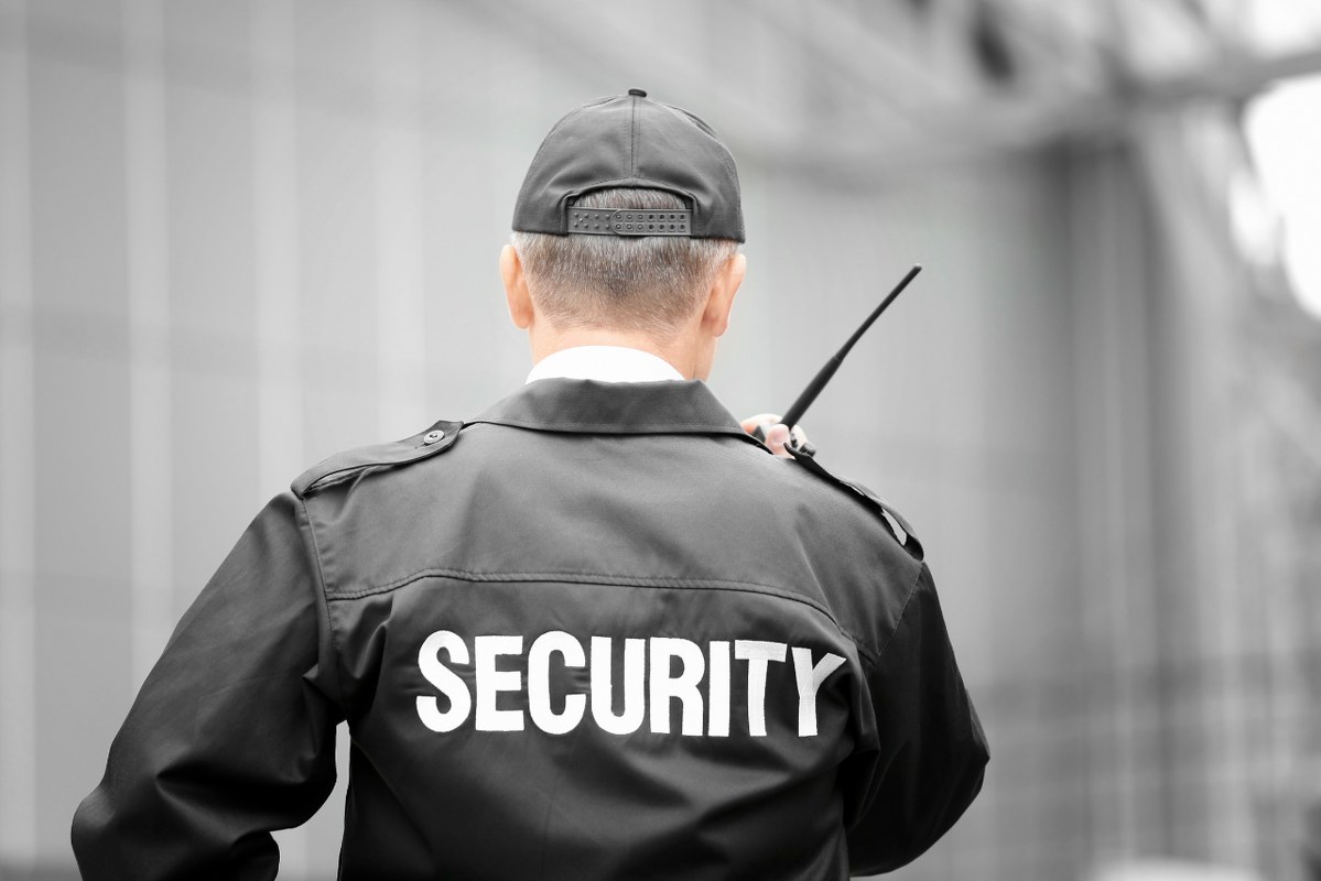 Backview of male security guad using radio phone outdoors.