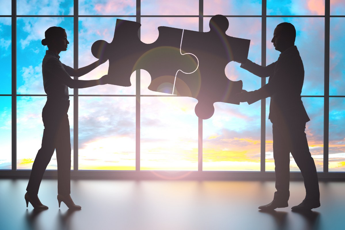Business partners connecting two puzzle pieces inside office.