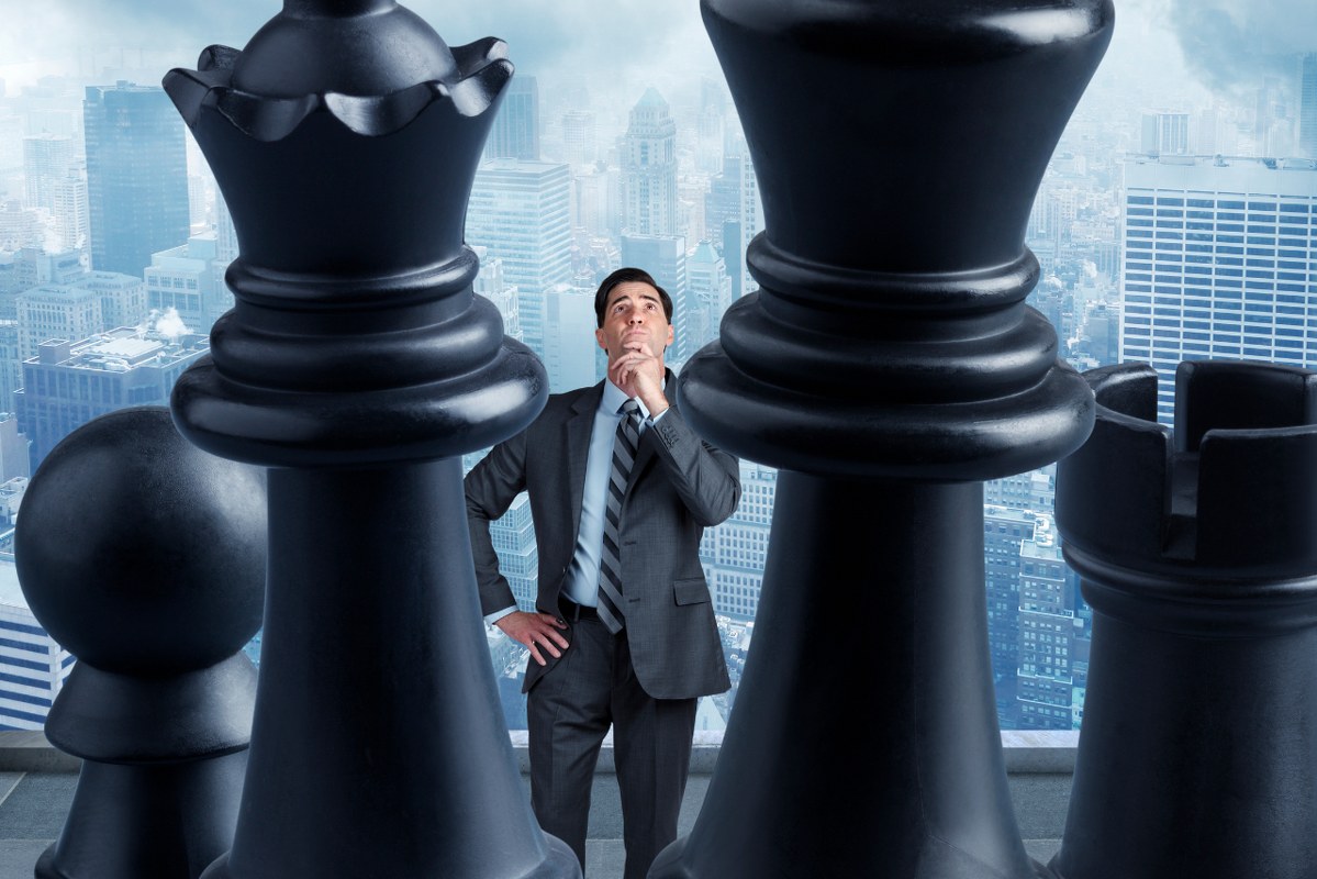 Businessman Looking Up At Chess Pieces.