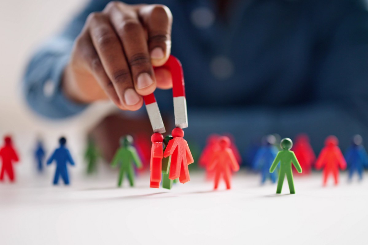 Close up of hand holding magnets to attract people figurines.