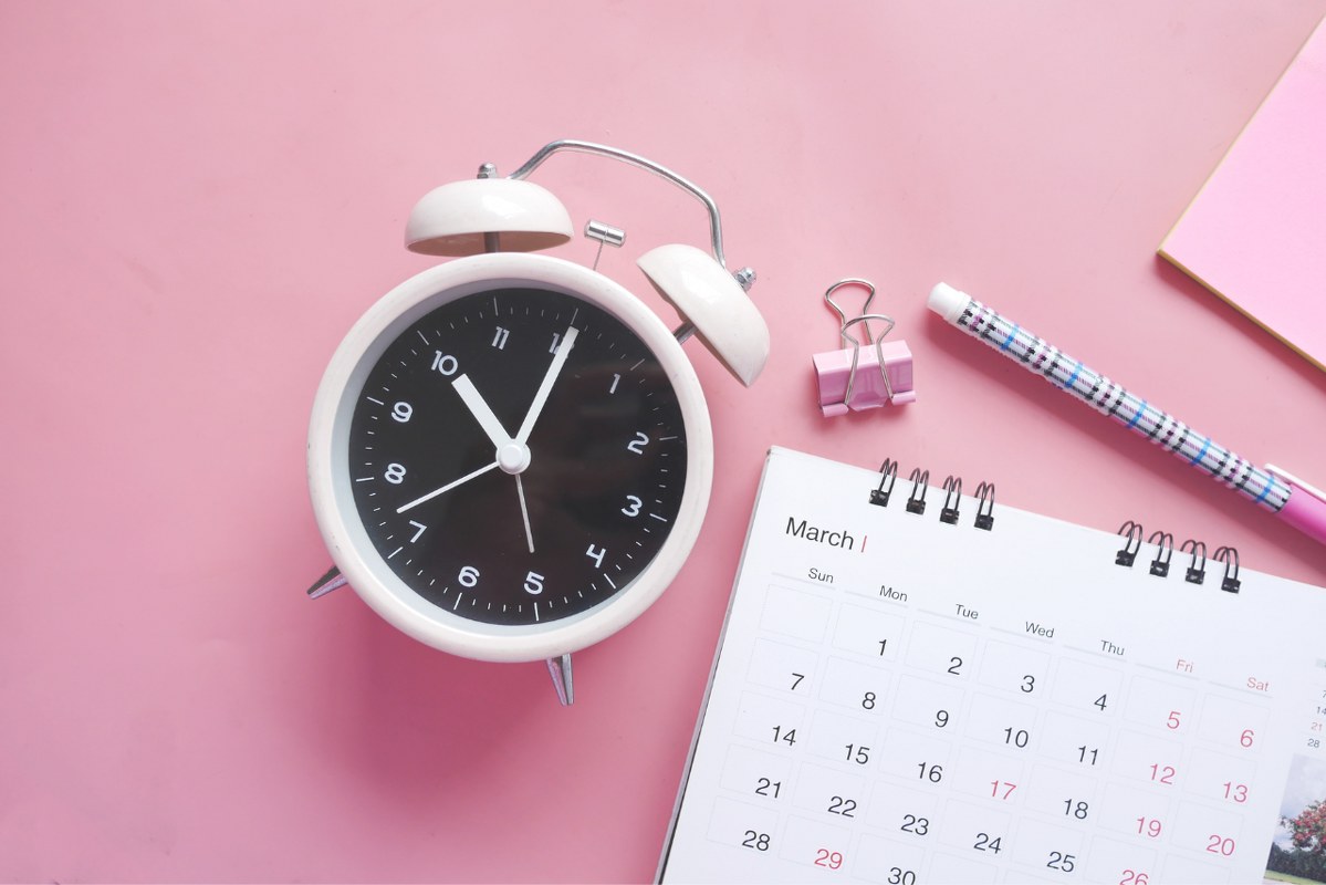 Close-Up Shot of an Alarm Clock and a Calendar on a Pink Surface.