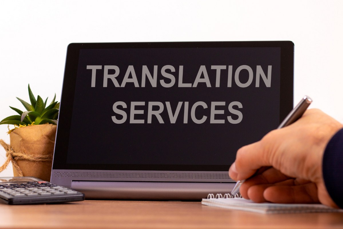 Close up of hand writing on paper with tablet screen written translation services.