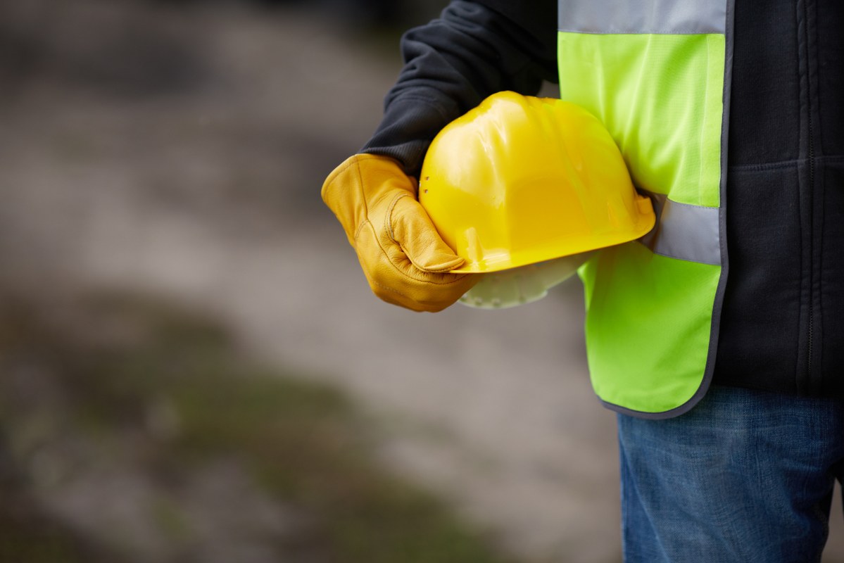 Construction Worker holding yellow hard hat and working gloves on site.