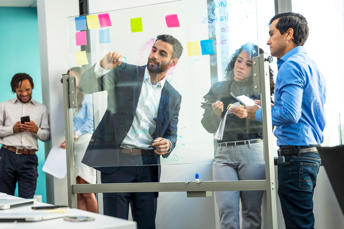 Consultant writing on transparent board and leading team.