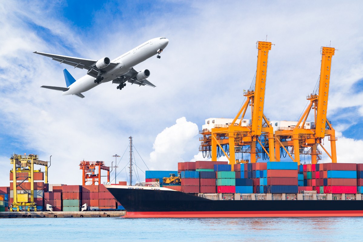 Container freight ship with plane flying above it.