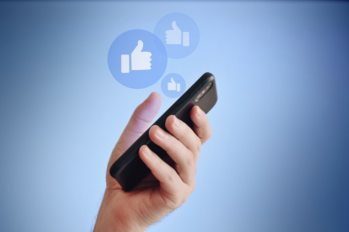 Crop hand holding phone while sharing on social media with likes.