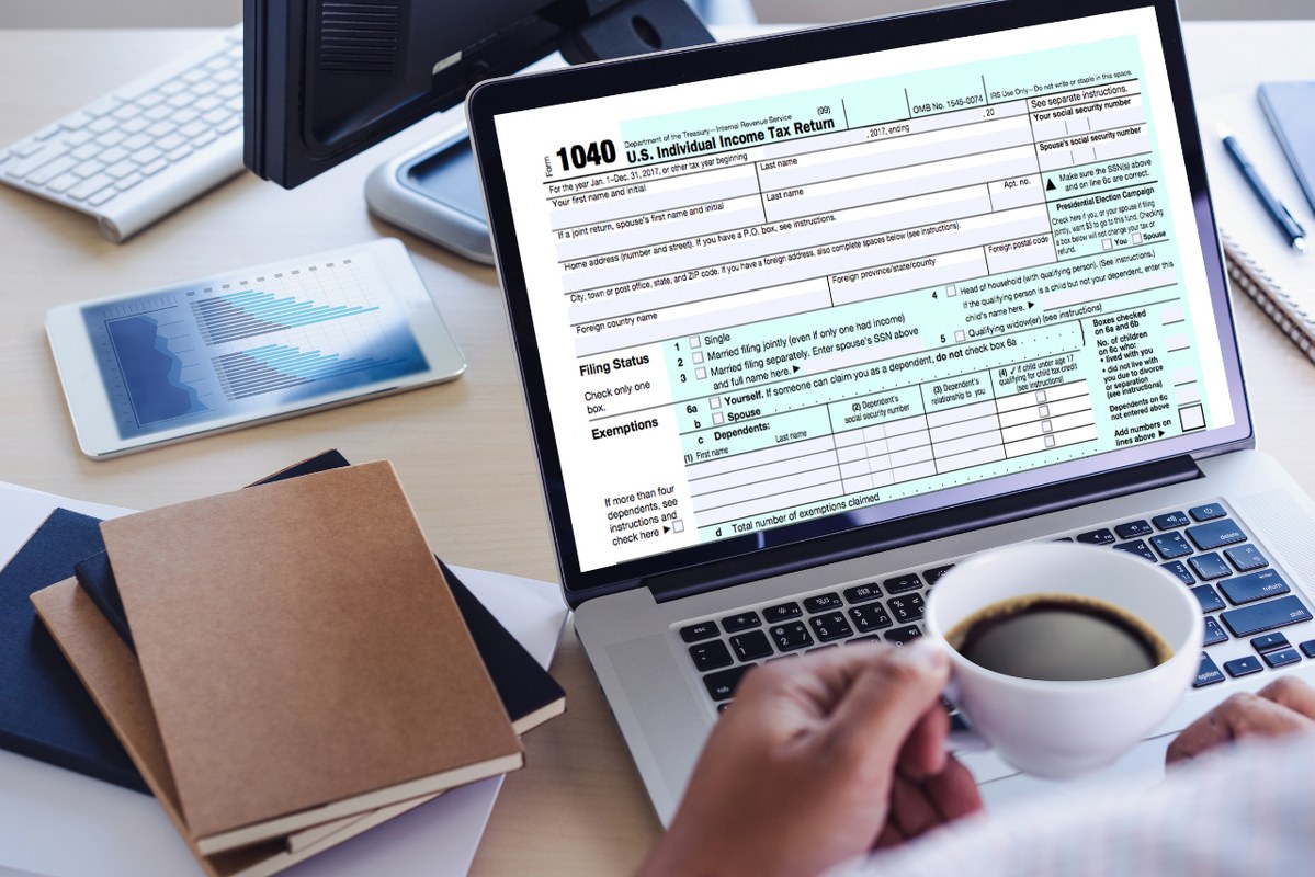 Financial accountant sipping coffee while doing taxes on laptop.