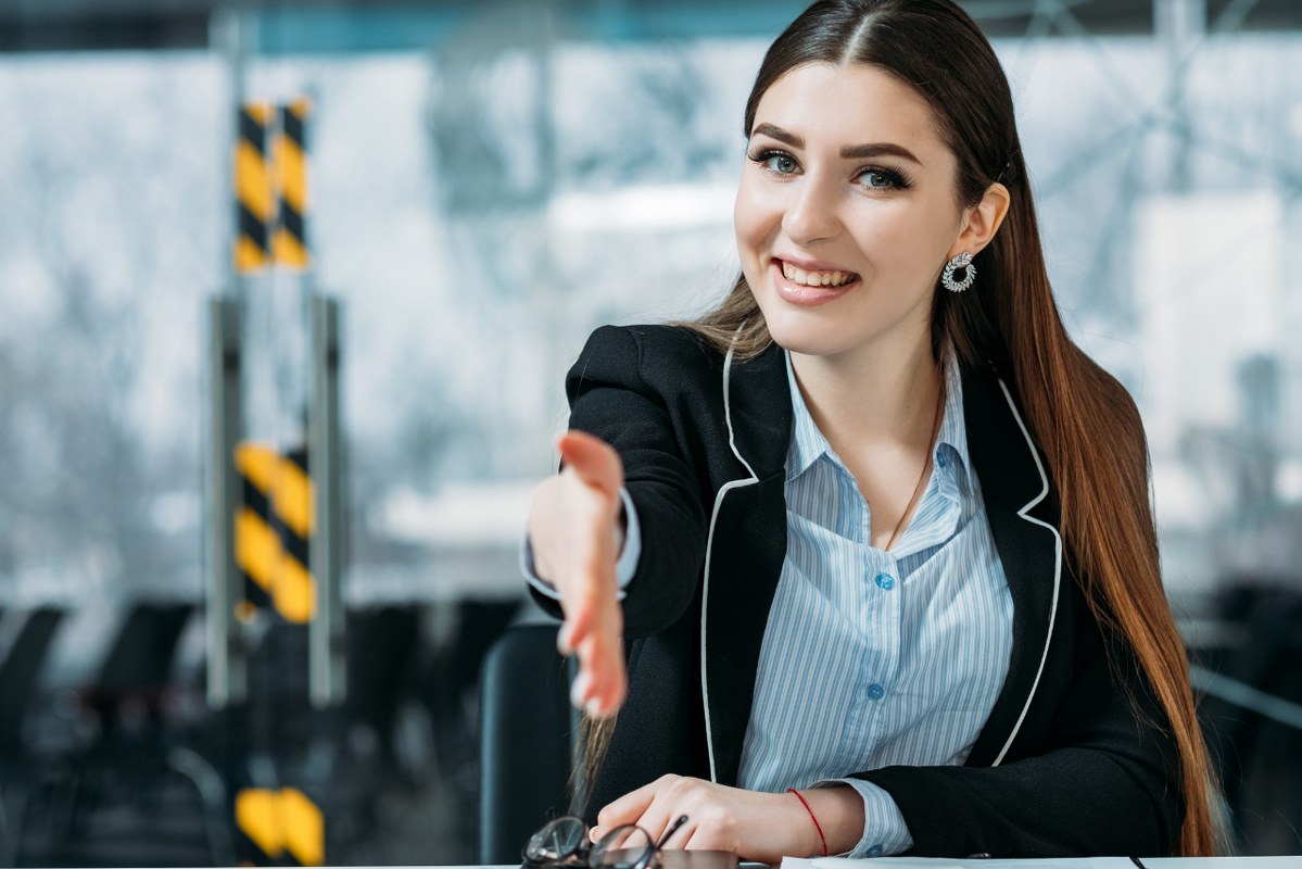 Friendly female salesperson smiling with a welcoming hand.