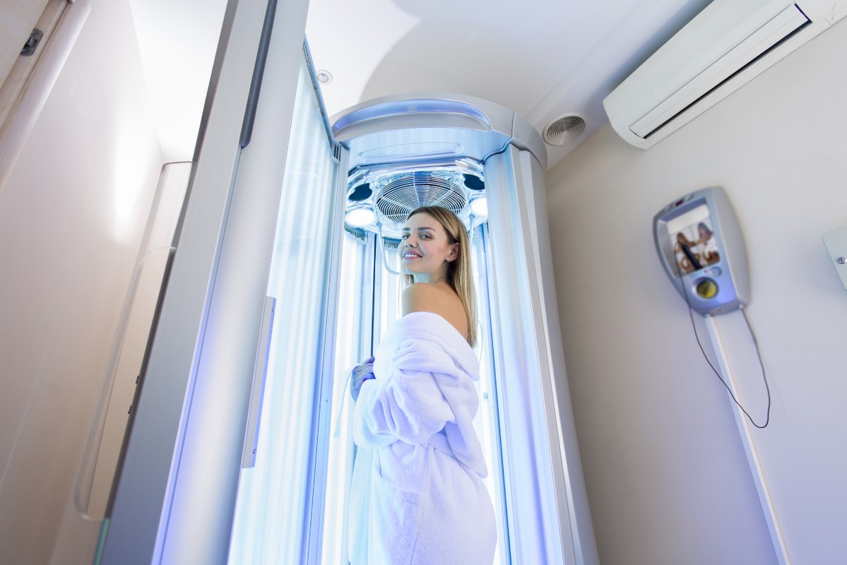 Girl in a White Robe Preparing for the Tanning Procedure in vertical UV bed.