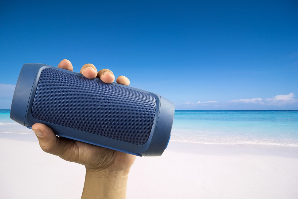 Hand holding portable speaker at the beach.