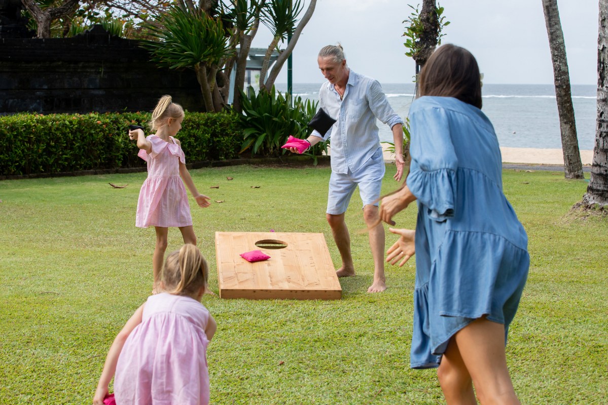 Happy family playing cornhole game outdoor on sunny summer day.