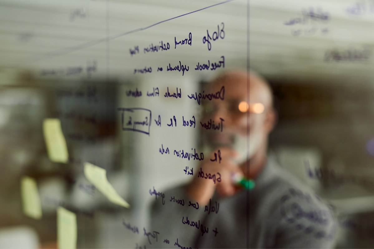 Male owner carefully thinks of business plan and writes it on transparent wall.