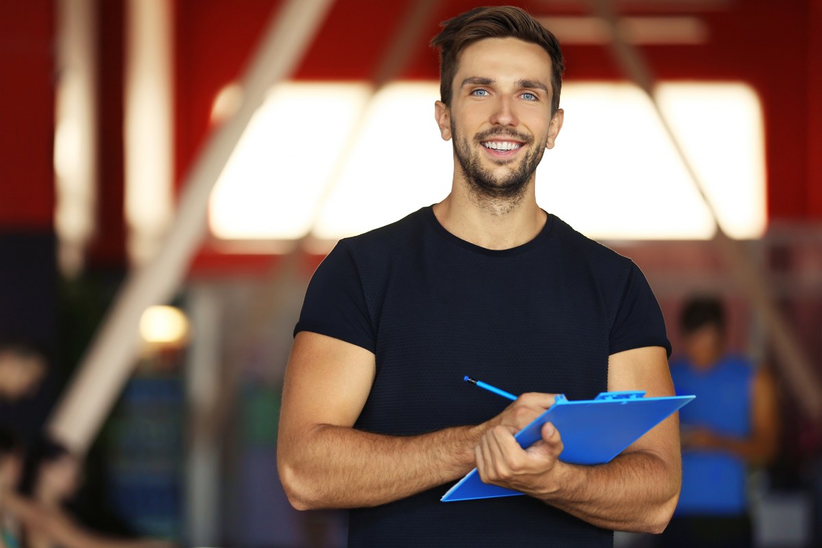 Male personal trainer holding pen and clipfolder.