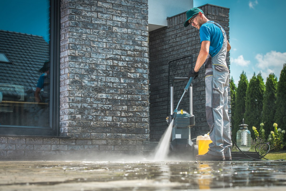 Male pressure washer is cleaning a dirty concrete floor.
