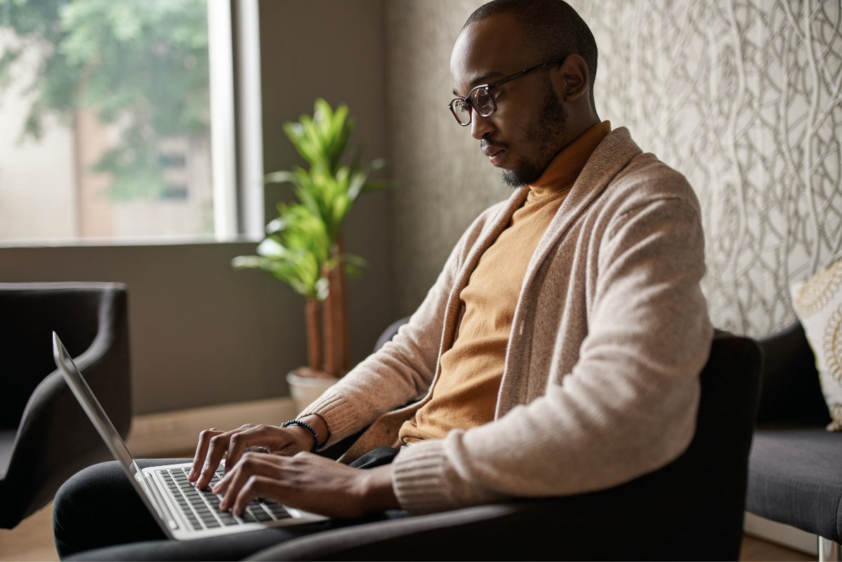 Male young writer sitting comfortably on chair while typing on laptop.