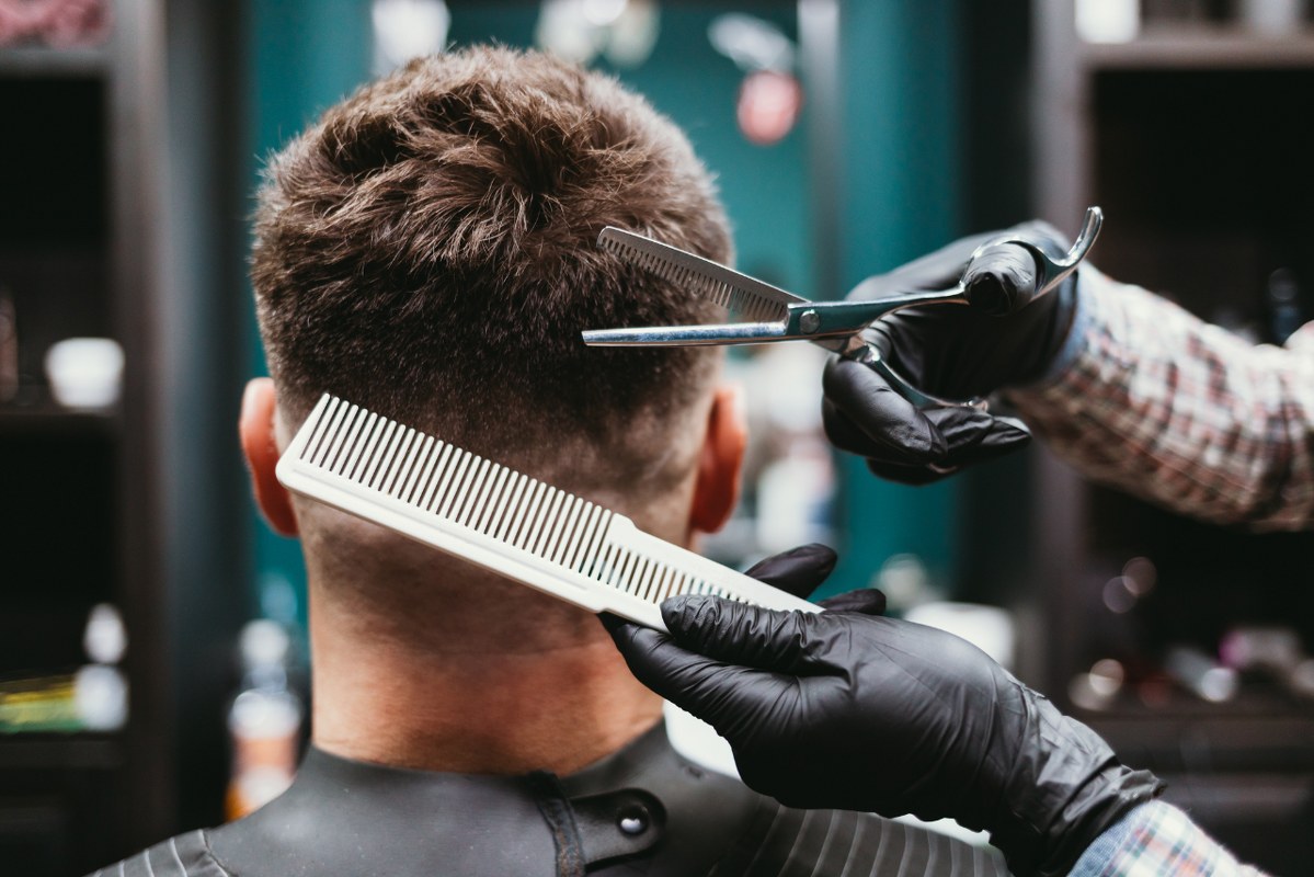 Man in Barbershop, close-up hairdresser making haircut to bearded male client.