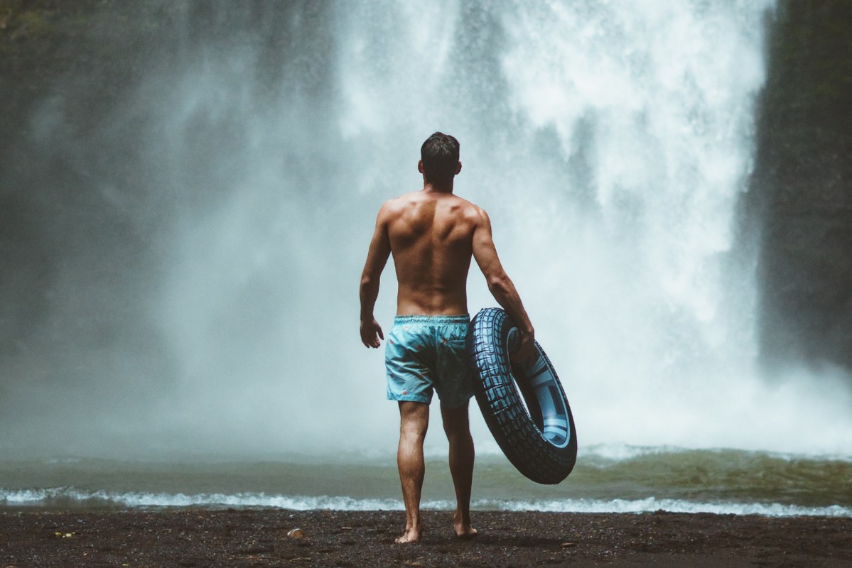Man in Swimming Trunks Facing a Big Waterfall.
