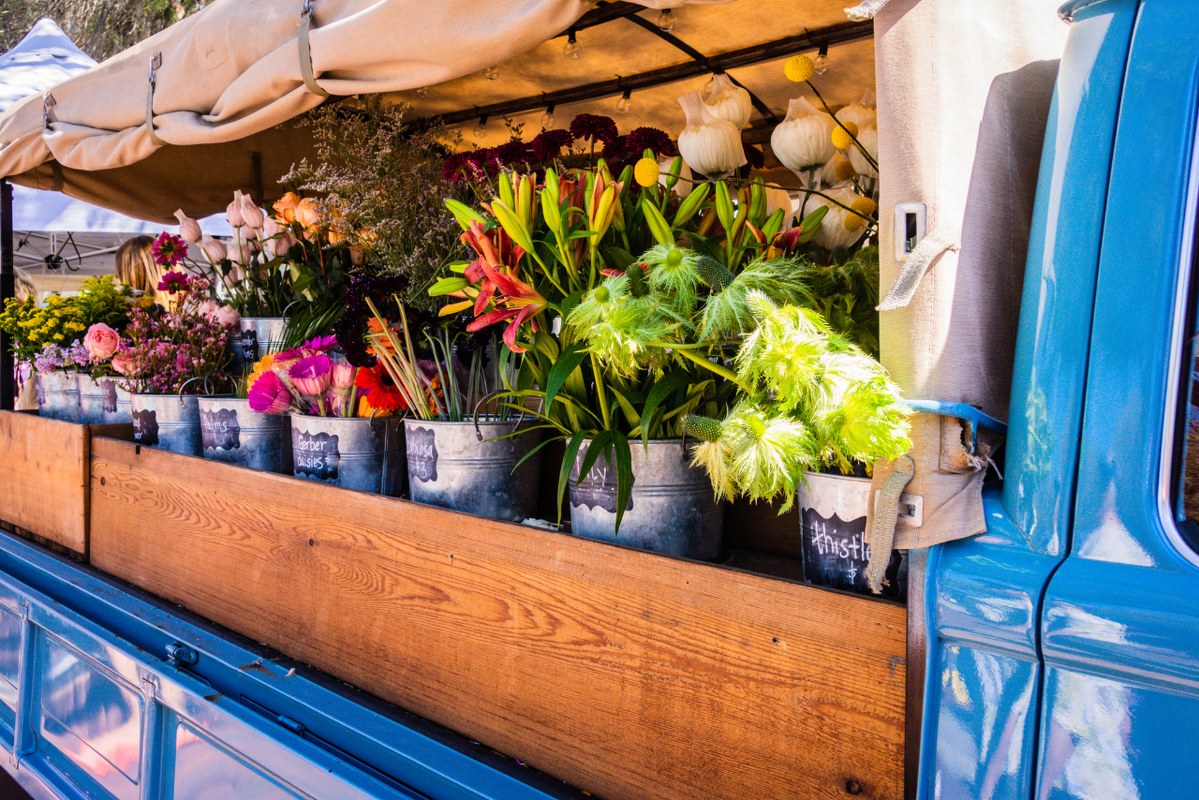 Open truck with buckets of flowers for sale.