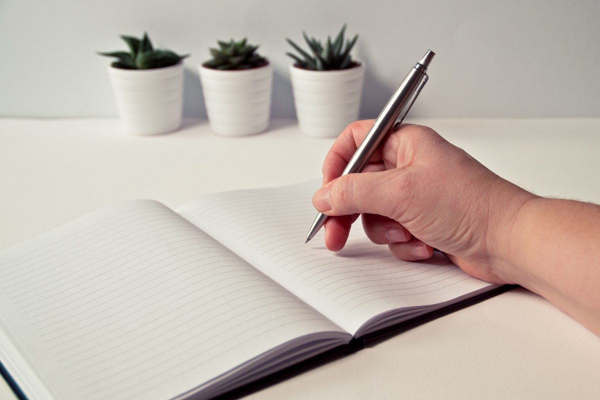 Person Holding Silver Retractable Pen in White Ruled Book.