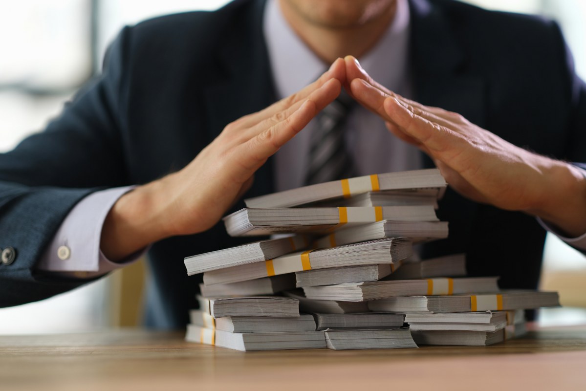 Person forming a protective shield using hands to cover stack of dollar bills.