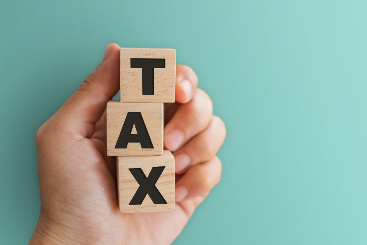 Person's Hand Holding Tax Word on Wooden Cubes.