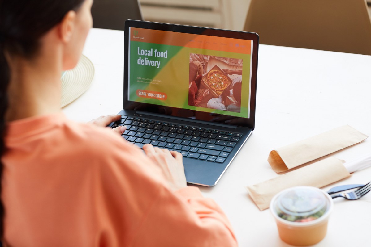 Rearview of woman sitting at table, infront of laptop ordering locally.