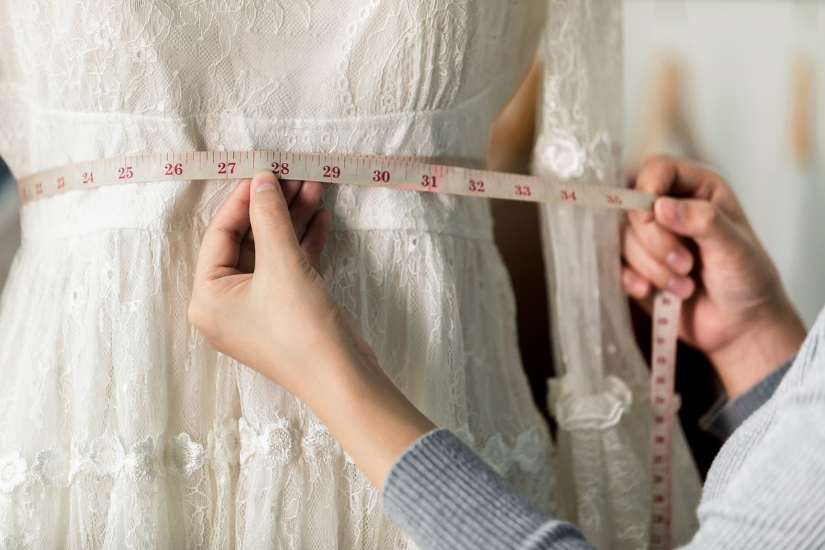 Seamstress Using a Tape Measuring Waistline of a White dress.