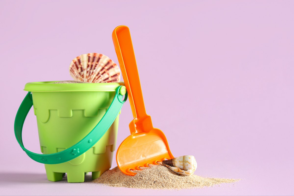 Seashells, Sand, Toy Shovel and Bucket on Lilac Background.