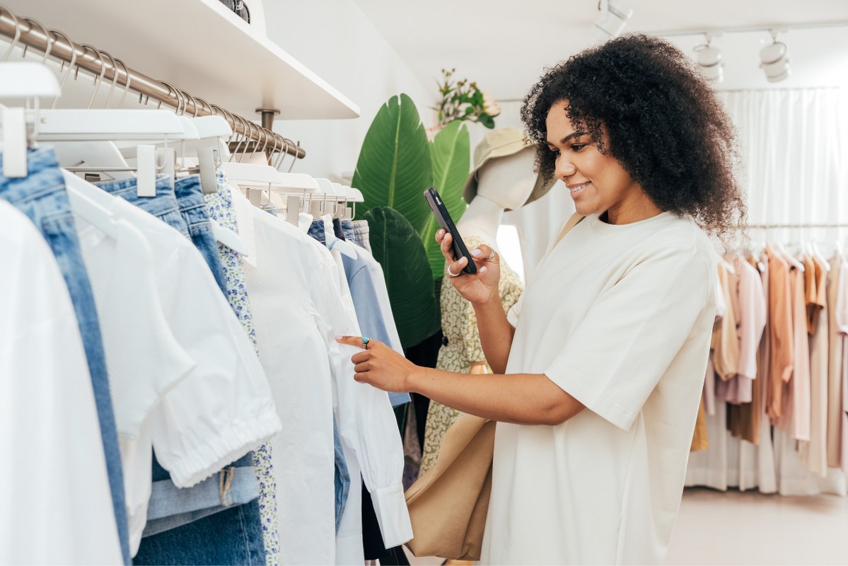 Side View of Young Woman Photographing Clothes in Shop.