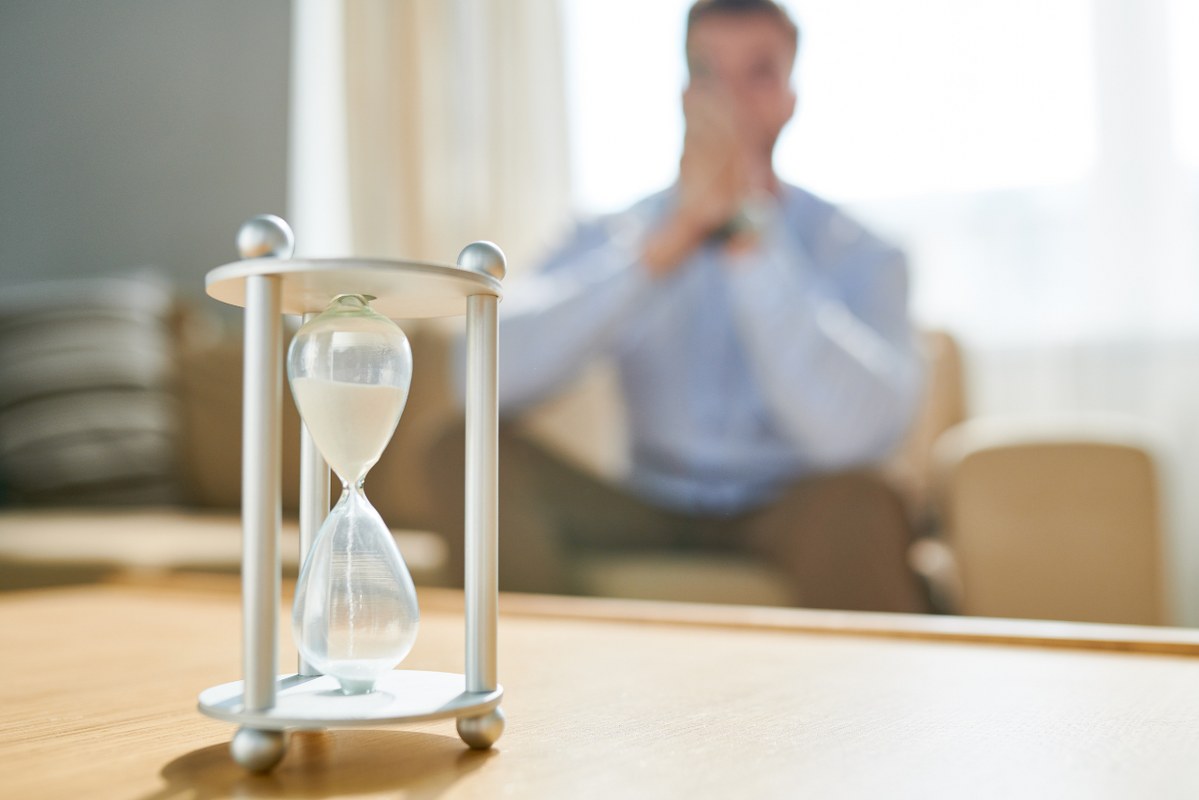 Takes time concept: Male person waits while looking at hour glass.