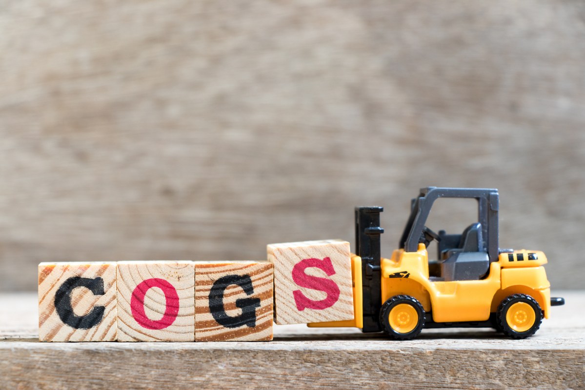 Toy forklift hold letter block S in word COGS (Abbreviation of Cost of goods sold) on wood background.