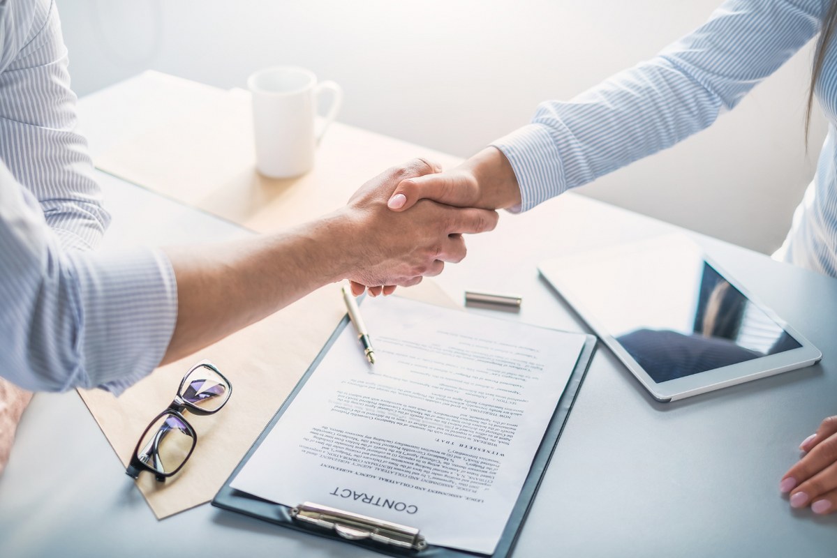 Two People shaking hands with contract on the table.