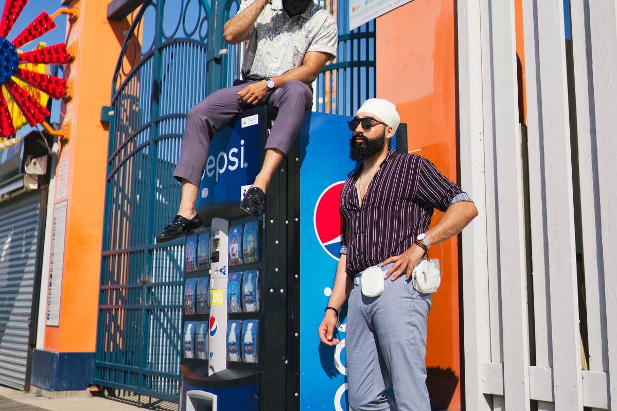 Two men sitting and standing behind snack machine.
