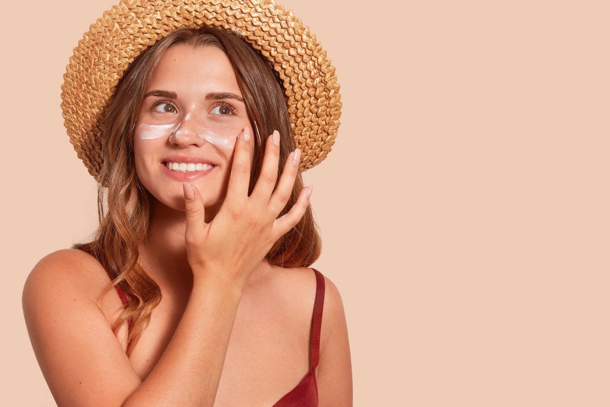 Woman Applying Sunscreen on Beige Wall.