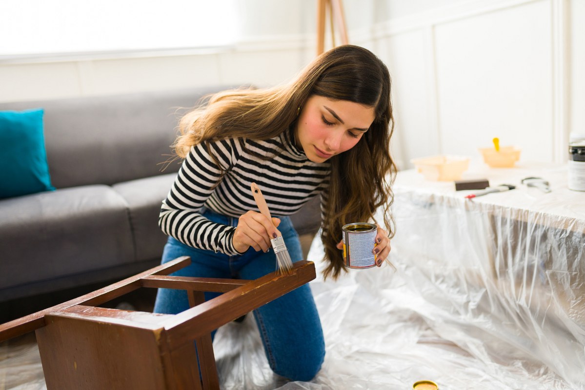 Woman applying varnish to wooden chair.