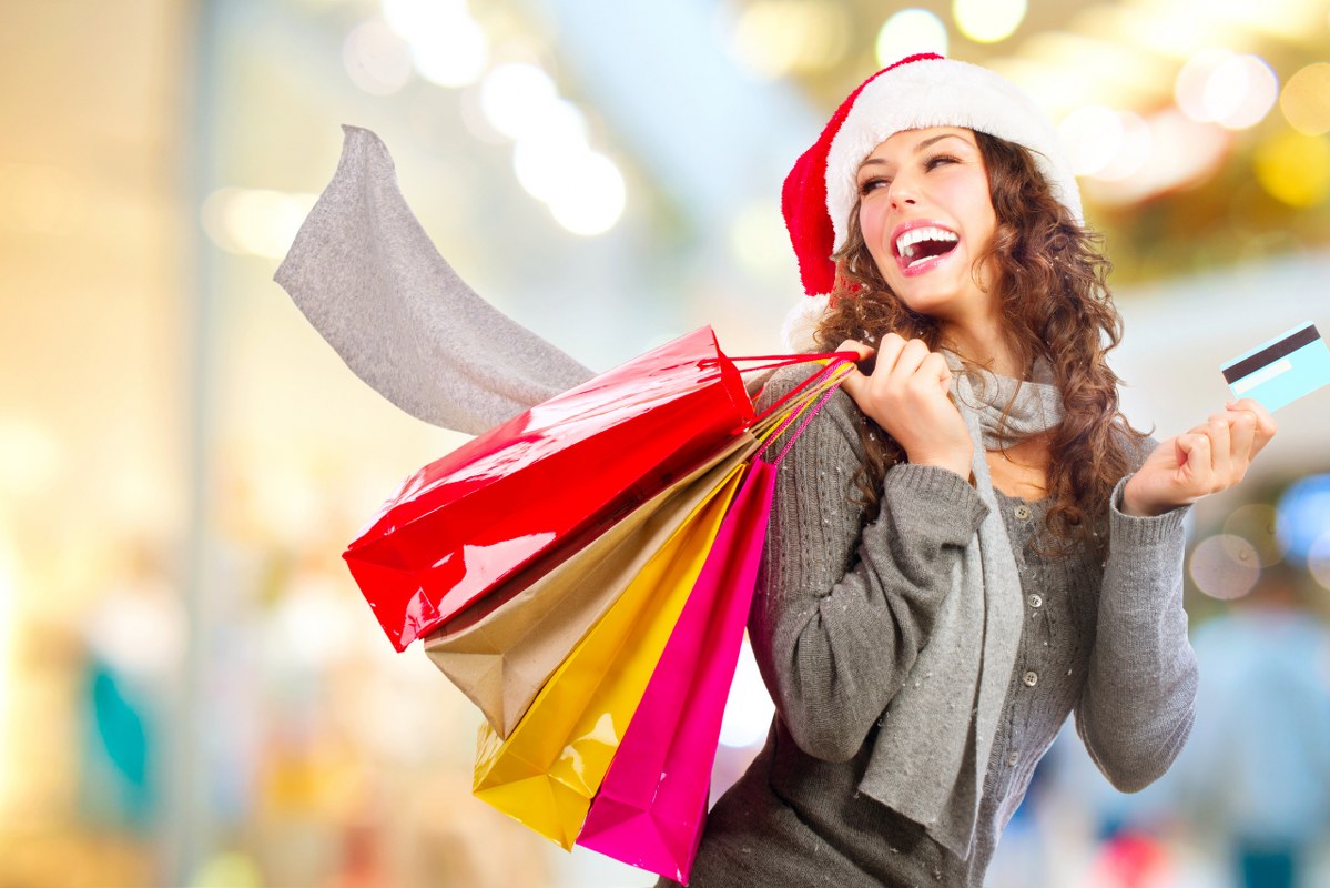 Woman excitedly carries shopping bags while wearing christmas hat and credit card.