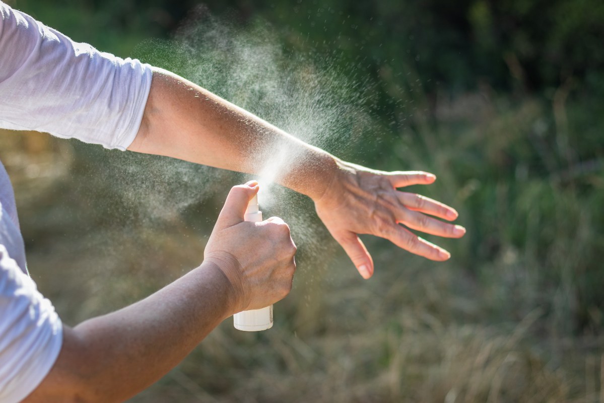 Woman spraying insect repellent on hand.
